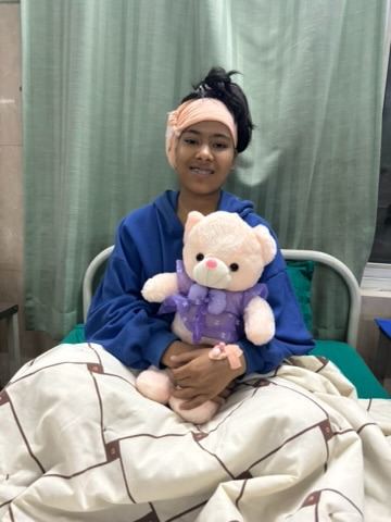 Bandana recovering in her hospital bed after ear surgery, holding a teddy bear