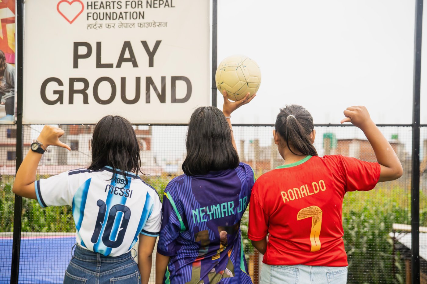 Three girls in Messi, Neymar Jr. and Ronaldo jerseys at the Hearts for Nepal playground