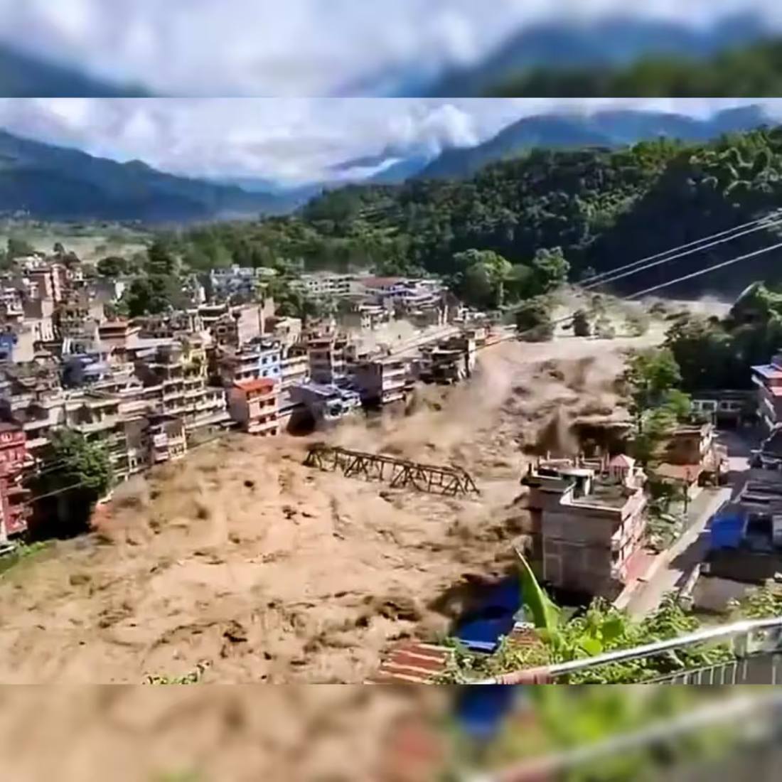 Floodwater and debris sweeping through a Nepal town, destroying buildings and a bridge