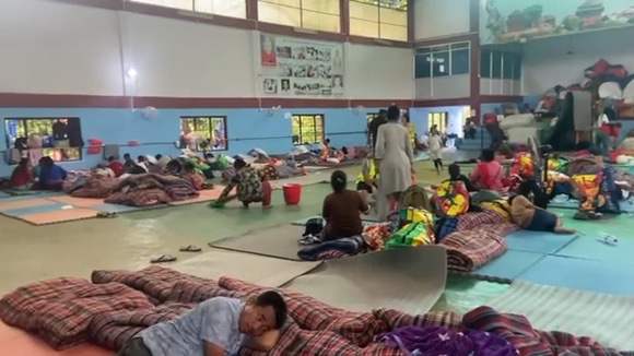 Displaced families sheltering on mats inside a community hall